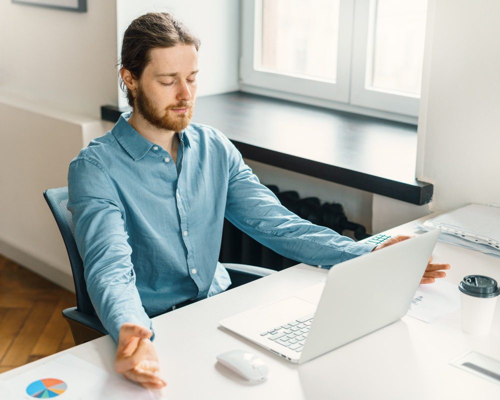 Calm male office worker meditating with closed eyes at work