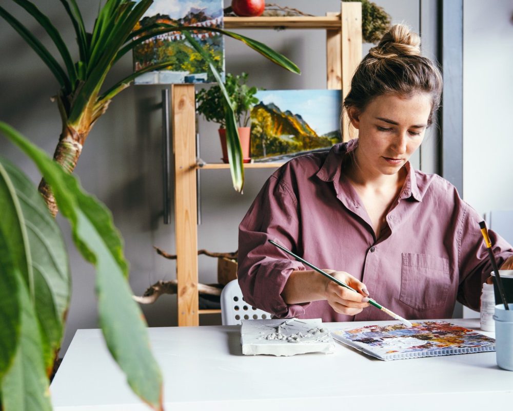 Young woman drawing in art studio with a lot of green plants. Arts and hobby concept.